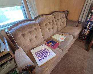 Vintage French Provincial style sofa with carved dark wood trim rail, button-tufted back cushions, and rolled arms in a brown chenille fabric; artist newsprint pads and office supplies shown on the seat are also available.