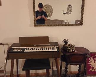 Electric home organ with matching bench, positioned beneath an ornate gold-framed wall mirror.