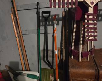 Long-handled yard tools including shovels and rakes, leaning against the garage wall beneath a decorative wood cross.