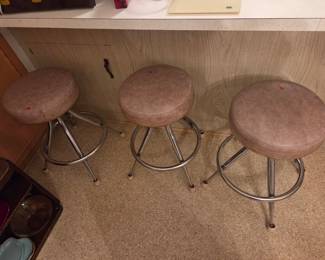 Set of three chrome-legged swivel bar stools with round padded seats, tucked under the kitchen counter.