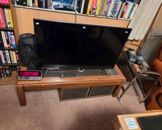 Flat-screen television on a wood media console with cabinet storage, beneath a bookshelf filled with books.