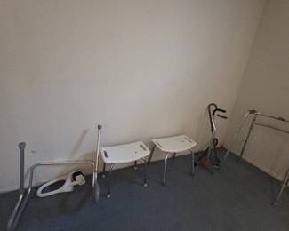 Collection of mobility and bath safety equipment including two plastic shower benches, an adjustable aluminum folding walker, a toilet safety frame, wooden and metal canes including a quad-style cane seat, and a bed rail assist.