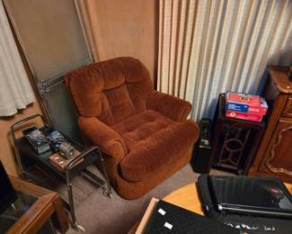 Rust-colored upholstered recliner, shown beside a small metal cart and a wood nightstand.