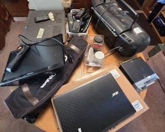 Table of electronics including an Acer laptop with Intel processor, a Proscan portable TV/DVD player with remote, a Sony portable boombox, a flatbed scanner, cordless phones and remotes, a Sony component, and a Vanguard tripod carry bag.