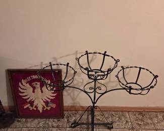 Wrought iron three-tier plant stand, shown beside a decorative red wall plaque featuring an eagle emblem.
