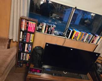 Same television area showing a wood VHS storage tower and a row of books along the windowsill.