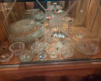 Close-up of the same cabinet's bottom shelf, packed with clear pressed and cut glass bowls, plates, and dishes.