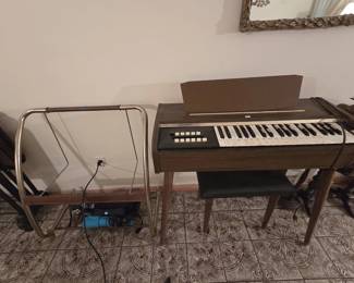 Vintage Silvertone electric chord organ in a walnut-tone case with tapered mid-century legs, shown with bench. A brass finish rolling valet rack sits beside it.