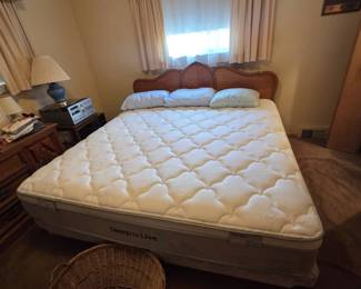 Bedroom featuring a king size bed with French Provincial carved wood headboard, a Sleep to Live Series 300 pillow-top mattress and box spring, striped pillows, and a large woven wicker laundry basket at the foot of the bed.