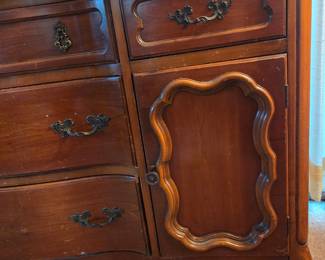Close-up of the same dresser's side drawers and scalloped decorative door panel with brass pulls.
