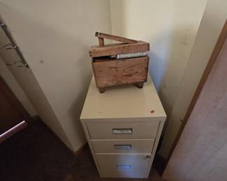 Vintage dovetailed wooden shoeshine box with angled footrest, sitting on a cream metal three-drawer locking file cabinet.
