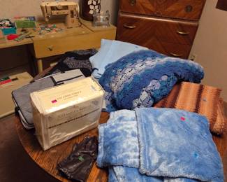 Assorted folded blankets and throws displayed on a round table, near the same highboy dresser.