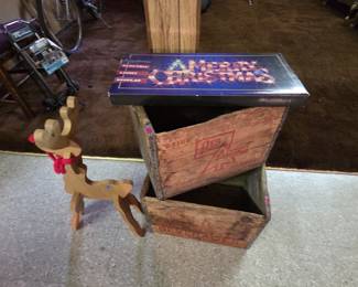 Two vintage wooden advertising soda crates, one stamped Drink Red Arrow 32 oz in red lettering, great for storage or display. Shown with a boxed electric Merry Christmas light-up sign and a handmade wooden scroll-cut reindeer with a red cord collar.