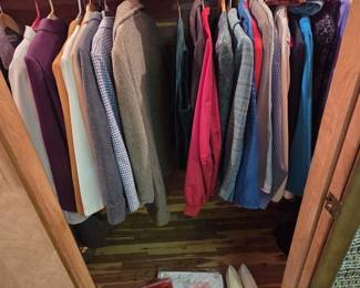 Cedar-lined closet of vintage mens and ladies clothing including tweed and houndstooth sport coats, blazers, dress shirts, and colorful jackets, with two red Club Filarets snapback caps on the shelf, cream leather pumps, garment bags, and a quilted dress cover.