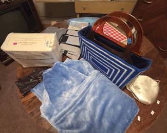 Vintage handbag and linens grouping featuring a blue and white geometric woven tote with amber lucite handles, a gold metallic clutch, brown leather gloves, a plush blue throw, and a factory-sealed 300 thread count luxury sateen king 6-piece sheet set.