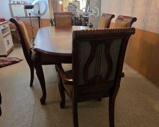 Same oval wood dining table and cane-back chairs viewed from another angle, in a wood-paneled dining area with a hutch and storage baskets visible in the background.