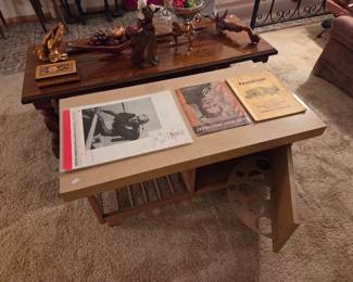 Low wood media table with a film-reel cutout side panel and a lower shelf of vinyl records, shown with vintage movie prints displayed on top.