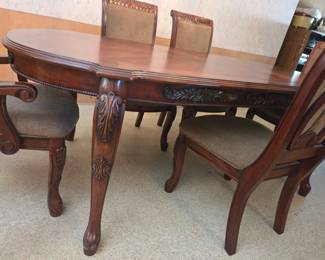 Closer view of the same dining table's carved apron and cabriole legs with acanthus-leaf detailing, alongside upholstered chairs.