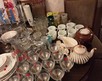 Same table covered with stemmed glassware, cups, and a ceramic teapot.