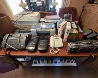 Office and music electronics grouping: a Sharp fax machine, a JETYD JU-303 handheld unit, a white desk telephone, a General Electric AM/FM cassette boombox, HP all-in-one printers, sealed Microsoft Office 2000 and Project 98 software, a Super 8 movie light in the box, keyboard carrying case, and a full-size electronic piano keyboard.