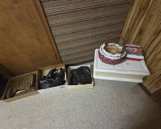 Ladies boots in original boxes including tan quilted winter boots and two pairs of black leather fashion boots, alongside two white storage totes topped with a Christmas fabric-wrapped handled basket and a holiday village tin.