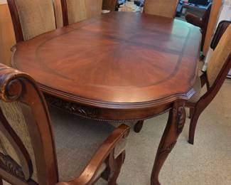 Dining table with a scalloped edge and cabriole legs, paired with upholstered chairs in tan fabric, in a room adjoining the living area.