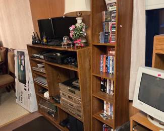 Wood bookshelf and media unit holding movies and games, with a computer monitor and FAMILY wall decor nearby.