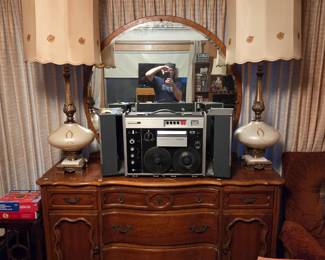 Same stereo system centered on a dresser, flanked by a pair of matching table lamps beneath an oval mirror.
