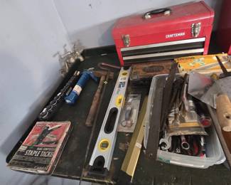 Craftsman portable metal toolbox with drawers, alongside a Stanley FatMax box level, socket set, caulk gun, sledge hammer, pry bar, a Sears Craftsman dual compression staple tacker in its original box, and a bin of combination wrenches and hand tools on a workbench.