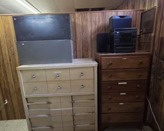 Mid-century blonde chest of drawers with sculpted metal pulls and louvered-front lower drawers, beside a solid wood six-drawer lingerie chest; a compact stereo system with speakers and a vintage radio sit on top.
