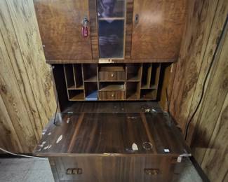 Art Deco waterfall-front secretary desk in figured walnut veneer, with a drop-front writing surface opening to a fitted interior of pigeonholes and small drawers, twin locking cabinet doors flanking a center mirror, and two lower drawers; veneer loss noted, a solid candidate for restoration.