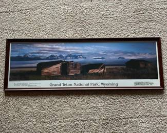 eh- This framed panoramic photograph by Leo L. Larson captures the majestic landscape of Grand Teton National Park in Wyoming, featuring the iconic Pfeiffer Homestead and Teton Range in the background. The image is printed with a rich color palette that highlights the natural beauty of the wild country, including the deep blues and purples of the sky and mountain range, against the rustic wooden homesteads and golden field. Framed in a classic dark brown wood frame with a smooth, glossy finish, making it an ideal decorative element for nature enthusiasts and collectors of scenic art. The print also includes an inspirational quote about the rugged wilderness and the spirit of hope, adding thoughtful context to the artwork.