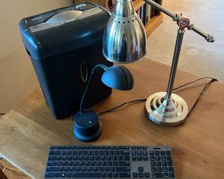 md- This office set features a powerful black paper shredder with a separate waste bin, a slim modern black and silver wired keyboard, and two versatile desk lamps. The first lamp is a sleek black design with a curved neck and dome-shaped shade, ideal for focused task lighting. The second lamp showcases a polished silver metal finish with an adjustable arm and a conical shade, perfect for adjustable illumination. Together, these items provide functional and stylish lighting and office tools suitable for any workspace. Shredder: L: 12in W: 7in H: 15in Keyboard: 17in x 4in Black Lamp: H: 19in Silver Lamp: H: 21in