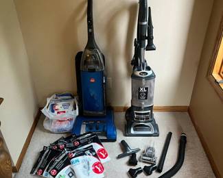 ir- This set includes two upright vacuum cleaners, featuring a blue Hoover model and a silver Shark XL capacity model. Both vacuums come with multiple attachments such as various nozzles, brushes, and hoses, enhancing their cleaning versatility. Additionally, the package includes a large assortment of replacement vacuum bags and filters compatible with Hoover models, ensuring long-lasting maintenance.