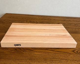 kn- This Chef's Cutting Board features an all-wood construction, offering a sturdy and reliable surface for all your food preparation needs. Crafted from natural wood, it highlights a smooth, polished finish with a light wood tone that complements any kitchen décor. Measuring approximately 18 inches in length and 12 inches in width, this cutting board is generously sized for versatile cutting tasks. The board also includes a convenient hand grip on the side for easy lifting and handling. Perfect for chefs and home cooks seeking a durable, aesthetically pleasing cutting surface.