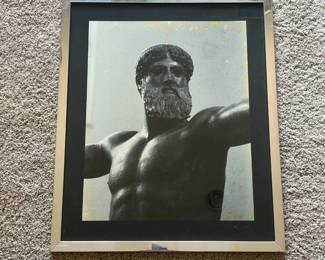 dg- This framed black and white photograph features a detailed close-up of a classical male statue showcasing muscular torso and bearded face with an outstretched arm. The piece is highlighted by a sleek silver metallic frame that adds a modern touch to the classical imagery. The photograph is matted with a black border, enhancing its contrast and visual appeal. The frame shows some wear and patina with minor scratches and marks, adding a vintage character to the item. The back has a hanging wire for easy wall mounting. Ideal for enthusiasts of classical art or those seeking a striking monochrome decor element.