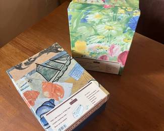 lw- This set includes two unique photo and video storage boxes, each featuring distinct and colorful designs. One box showcases a lively floral pattern with green, yellow, pink, and blue hues, resembling a vibrant garden scene. The other box is adorned with artistic illustrations including seashells, sails, and assorted paper elements in a palette of beige, blue, orange, and black. Both boxes are made from sturdy materials suitable for organizing and protecting photos and videos. The interiors are spacious with plain white lining, ideal for easy labeling and storage. Measuring approximately the same size, these boxes combine functionality with artistic flair, perfect for those who appreciate practical storage solutions infused with creativity and color. L: 11in W: 8in H: 5in