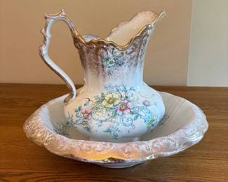 aw- This elegant porcelain wash pitcher and basin set features intricate floral designs complemented by luxurious gold trim. The pitcher stands 14 inches tall and is 9 inches wide, while the basin measures 4.5 inches in height and 15.5 inches in width. Both pieces showcase a classic vintage style with delicate patterns and a sophisticated finish, making them perfect decorative accents or functional collectibles. Made by Alliance.