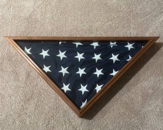 bx- This elegant triangular display case is designed to house and showcase a folded American flag, typically used for memorial or ceremonial purposes. It features a sturdy wooden frame with a natural finish that highlights the rich grain of the wood. The front is protected by a clear glass cover, allowing the white stars on the navy blue flag to be prominently displayed. The case's solid back panel ensures secure support while maintaining a classic and respectful appearance. Perfect for preserving and honoring a flag, this display case combines functionality with timeless craftsmanship. L: 25in W: 12.5in H: 3in