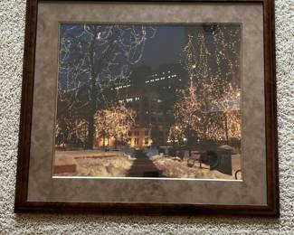 dw- Large framed color photograph depicting a snowy urban park illuminated by thousands of holiday lights, believed to show Rice Park in downtown St. Paul, Minnesota. Rice Park is well known for its winter and holiday light displays. The atmospheric nighttime scene features snow-covered walkways, benches, mature trees wrapped in lights and downtown architecture in the background. The photograph is professionally presented under glass with a wide taupe mat and substantial wood-tone frame. A label on the reverse identifies Kelley Frame & Fine Art Galleries, Ltd., with locations in Stillwater and Woodbury, Minnesota and Hudson, Wisconsin. Kelley Gallery has operated in the Twin Cities area since 1985 and specializes in artwork and custom framing.