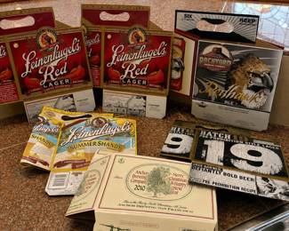le- This collection includes six assorted beer carriers showcasing unique branding from Leinenkugel's Red Lager and Summer Shandy, Rockyard's Redhawk Ale, Anchor Brewing Company with a 2010 Christmas and New Year design, and Batch 19 Pre-Prohibition Style Lager. Also an assortment of 22 coasters. Highlighting vibrant colors, distinctive logos, and various sizes tailored for six-pack bottles, these carriers are made of sturdy cardboard material, perfect for collectors or beer enthusiasts.