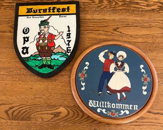 mr- This set includes a vintage Wurstfest 1976 shield featuring a colorful illustration of an Opa in traditional attire, marked with 'New Braunfels, Texas,' and a round wooden Willkommen plaque showcasing a lively folk dance couple against a rich blue background. The shield is painted with bold black, yellow, green, and red accents and has a rustic aged texture on the reverse side. The plaque is detailed with floral embellishments and warm wooden framing. Both items reflect German-Texan heritage and are perfect for collectors or as unique décor celebrating cultural festivities. Sheild: 12in x 10in Round Plaque: 12in