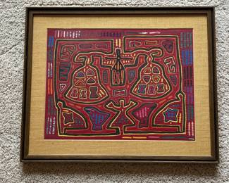 do- Colorful vintage mola textile panel, traditionally associated with the Guna people of Panama, presented under glass with a woven-texture mat and wood-tone frame. Molas are constructed from layered fabrics that are cut and hand-sewn to reveal contrasting colors and intricate designs, a technique commonly known as reverse appliqué. This example features a bold symmetrical composition in red, yellow, blue, green, orange and black, with stylized geometric and figural forms characteristic of Guna textile traditions. The reverse retains a Kemper Galleries, Colorado Springs, Colorado label noting custom framing. The piece is unsigned, as is common with many traditional mola panels. Presented in a substantial vintage wood frame with textured tan matting.