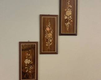 ep- This set of three wall panels features intricate floral inlay designs on rich, dark wooden backgrounds. Each panel showcases unique handcrafted flower motifs detailed in light, natural wood tones, creating a beautiful contrast with the deep brown wood grains. The panels are rectangular in shape, bordered with a delicate gold trim, and framed with a thicker, darker wood frame, enhancing their classic elegance. Perfect for adding a touch of vintage charm and artisanal craftsmanship to any room's décor.