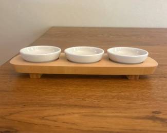 fr- This Longaberger dipping set features three small white ceramic bowls securely placed on a natural wood base, measuring approximately 13 inches in length and 4.5 inches in width. The bowls are about 3.25 inches in diameter, making them perfect for serving a variety of dips or condiments. Crafted with a combination of smooth ceramic and warm-toned wood, this set combines functionality with rustic charm, ideal for entertaining or everyday use.