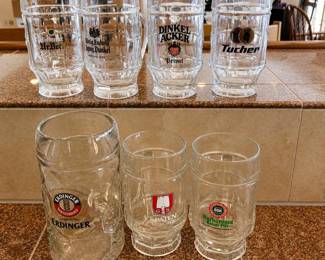 lh- This collection features 7 authentic German beer mugs, each showcasing logos from various renowned breweries including Eichbaum, Lepat Privat, Dinkel Acker, Tucher, Erdinger, Spaten Munchen, and Barbarossa. The set includes mugs ranging in size from approximately 6 to 6.5 inches in height with a diameter of 3.5 inches, plus one larger mug measuring about 8 inches tall by 4 inches in diameter. Crafted from clear glass, these mugs highlight detailed and colorful brewery logos, perfect for collectors or beer enthusiasts. Their varied sizes and iconic branding make them a unique addition to any bar or display.
