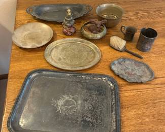 kz- This unique collection of antique collectables showcases a variety of vintage metalware, including intricately designed trays with floral and patterned engravings. Highlighted by their aged patina and decorative handles, the pieces vary in size and shape, featuring oval and rectangular trays alongside smaller items such as a brass cup, brush, and other vintage artifacts. The set exhibits a rich, rustic metal finish with hints of wear that emphasize their historical charm and authenticity.