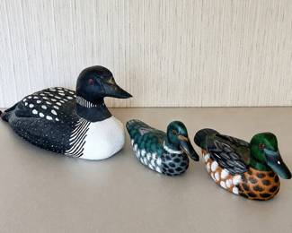 ae- Group of three hand-painted wooden waterfowl decoys featuring a large common loon and two smaller colorful duck decoys. The standout piece is the larger hand-carved and painted loon, with detailed black-and-white plumage and red eye. The underside is personally inscribed: It is dated 1/5/98 and signed Mark W. Nelson. The two smaller wooden ducks feature detailed hand-painted green, black, white and brown plumage. Their undersides are painted black; one retains remnants of an old label. No signatures are visible on the smaller ducks in the provided photos.