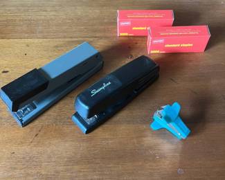 lr- This office supply set features two full-sized staplers in black and grey, each designed for reliable and efficient document fastening. Included are two boxes of standard red-packaged staples, each containing 5000 staples, suitable for frequent use. Additionally, a compact turquoise staple remover is part of the set, offering easy and damage-free staple removal. The staplers showcase sturdy metal construction with plastic accents, ideal for both home and office environments. The variety in size and the distinctive blue color of the staple remover highlight the complete and practical nature of this collection.