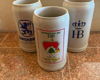 ll- This unique set of 3 stoneware beer steins includes distinct designs from Lowenbrau, HB, and a special Organization Day 23rd enamel insignia from 1964. Each stein stands 7.5 inches tall and measures 3.5 inches wide, crafted from durable stoneware with traditional coloring in neutral tones. Perfect for collectors or enthusiasts of vintage beer memorabilia, these steins showcase intricate logos and markings representing historic and celebratory themes.